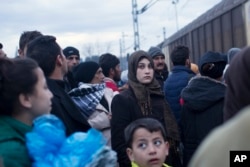 A woman stands in a crowd beside the railway tracks as a train passes beside a refugee camp where thousands of refugees are waiting to be allowed to cross the border into Macedonia in the northern Greek border station of Idomeni, Thursday, March 3, 2016.