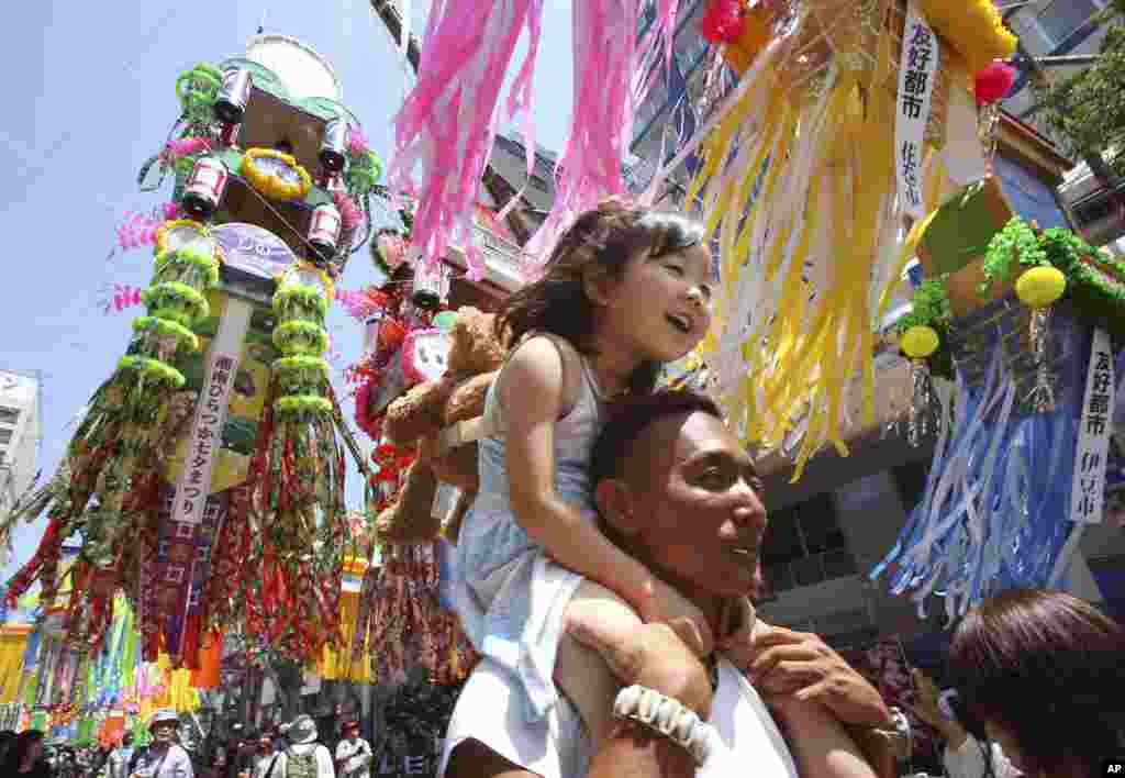 A girl is carried on her father&#39;s shoulder as people walk under colorful paper streamers decorated at a shopping street to celebrate the Tanabata Star Festival in Hiratsuka, near Tokyo. People celebrate the festival by writing wishes on strips of paper and hanging them under bamboo trees.