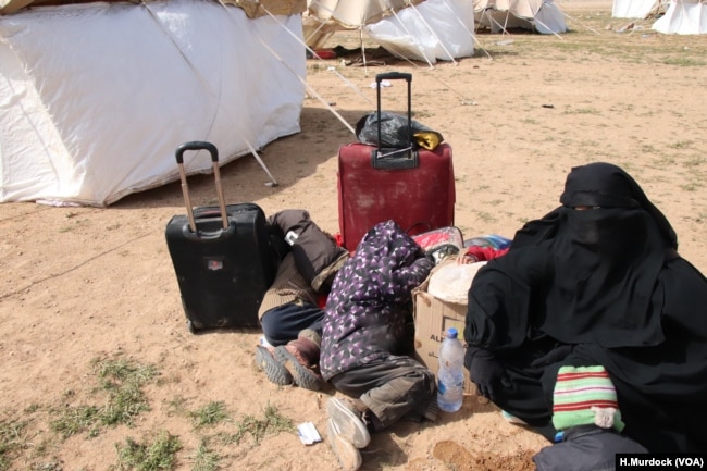 A woman, not knowing when or where she is going, waits with her children behind a collection of tents. "I don't know who I'm supposed to be afraid of, but I am afraid," she says, near Baghuz in Deir el-Zour, Syria, Feb. 26, 2019. (H.Murdock/VOA)