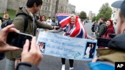 A Royal fan carrying a banner is interviewed by a member of the media, outside Windsor Castle in Windsor, south England, Monday May 6, 2019, after Prince Harry announced that his wife Meghan, Duchess of Sussex, has given birth to a boy. (AP Photo/Alastair Grant)