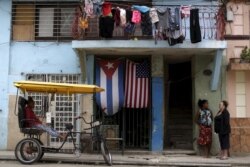 Perempuan terlihat di depan sebuah rumah berhiaskan bendera AS dan Kuba di pinggiran Havana, Kuba 21 Maret 2016. (Foto: REUTERS/Ueslei Marcelino)