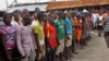 Residents of the Liberian capital, Monrovia stand behind a green string marking a holding area, as they wait for a second consignment of food from the Liberian government to be handed out, in the district of West Point, August 22, 2014