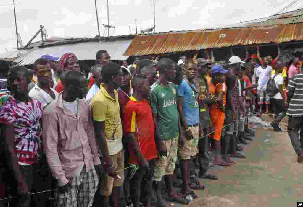 West Point residents stand behind a green string marking a holding area, as they wait for a second consignment of food from the Liberian Government, at the West Point area, Monrovia, Liberia, Aug. 22, 2014.