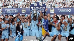 Kyaftin na kungiyar Manchester City, Vincent Kompany, a tsakiya dauke da kofin wasannin Lig na kasar Ingila, yayin da sauran 'yan wasan kungiyar suka kewaye shi lahadi 13 Mayu 2012, a filin wasa na Etihad dake Manchester, bayan da suka doke kungiyar Queen