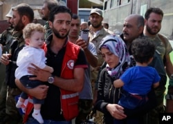 Staffers of the Syrian Arab Red Crescent assist families of gunmen as they leave from Al-Waer, the last rebel-held neighborhood of Homs, Syria, Sept. 22, 2016.