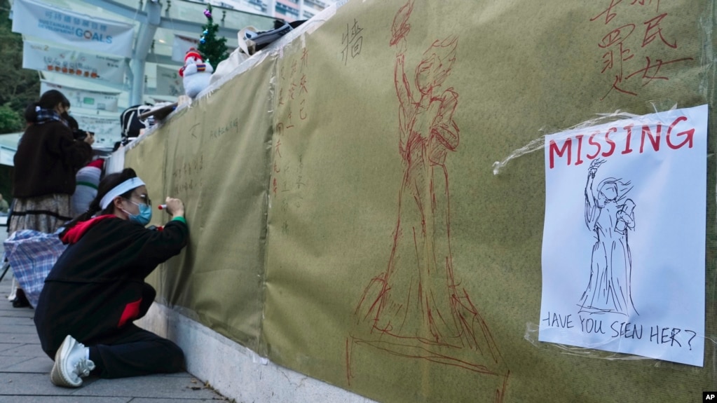 资料图片：2021年12月24日(星期五)，香港大学拆除纪念八九民运的“民主女神”雕像后，一名大学生在现场写下笔记。（美联社）(photo:VOA)