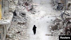 A woman walks past damaged buildings in the rebel-controlled area of Maaret al-Numan town in Idlib province, Syria, May 13, 2016.