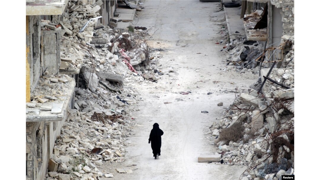 FILE - A woman walks past damaged buildings in the rebel-controlled area of Maaret al-Numan town in Idlib province, Syria, May 13, 2016.