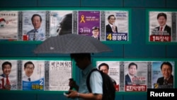 A man using his phone walks past election posters in Seoul, June 2, 2014.