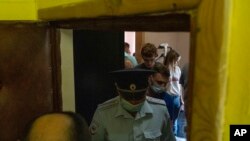 Polisi meninggalkan apartemen jurnalis Maria Zholobova (latar belakang, kanan) di Moskow, Rusia, setelah penggeledahan, Selasa, 29 Juni 2021. (AP Photo/Pavel Golovkin)