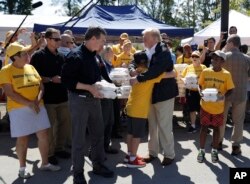El presidente Donald Trump y el gobernador de Carolina del Norte, Roy Cooper (izquierda) saludan a voluntariso mientras se preparan para repartir comida y otros insumos en un templo bautista, a afectados por el huracán Florence. Miércoles 18 de septiembre de 2018.