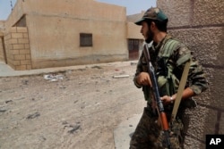 FILE - A U.S.-backed Syrian Democratic Forces fighter takes cover behind a wall on a street where they fight against Islamic State militants, on the front line on the western side of Raqqa, Syria, July 17, 2017.