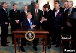 President Donald Trump, surrounded by business leaders and administration officials, gives the pen to Lockheed Martin CEO Marillyn Hewson after signing a memorandum on intellectual property tariffs on high-tech goods from China, at the White House.