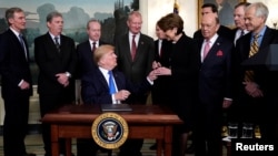 FILE - President Donald Trump, surrounded by business leaders and administration officials, gives the pen to Lockheed Martin CEO Marillyn Hewson after signing a memorandum on intellectual property tariffs on high-tech goods from China, at the White House, March 22, 2018. 