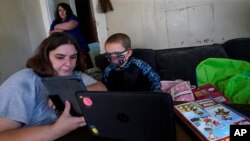 Christi Brouder, left, assists her son Wyatt, a kindergarten student with special needs, while her children distance learn due to the COVID-19 outbreak. (AP Photo/Charles Krupa)