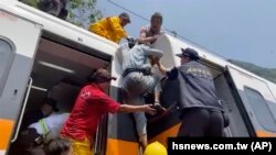 Des équipes de secours aident un passager, au centre, à sortir d'un train qui a déraillé dans le comté de Hualien, dans l'est de Taïwan, vendredi 2 avril 2021. 