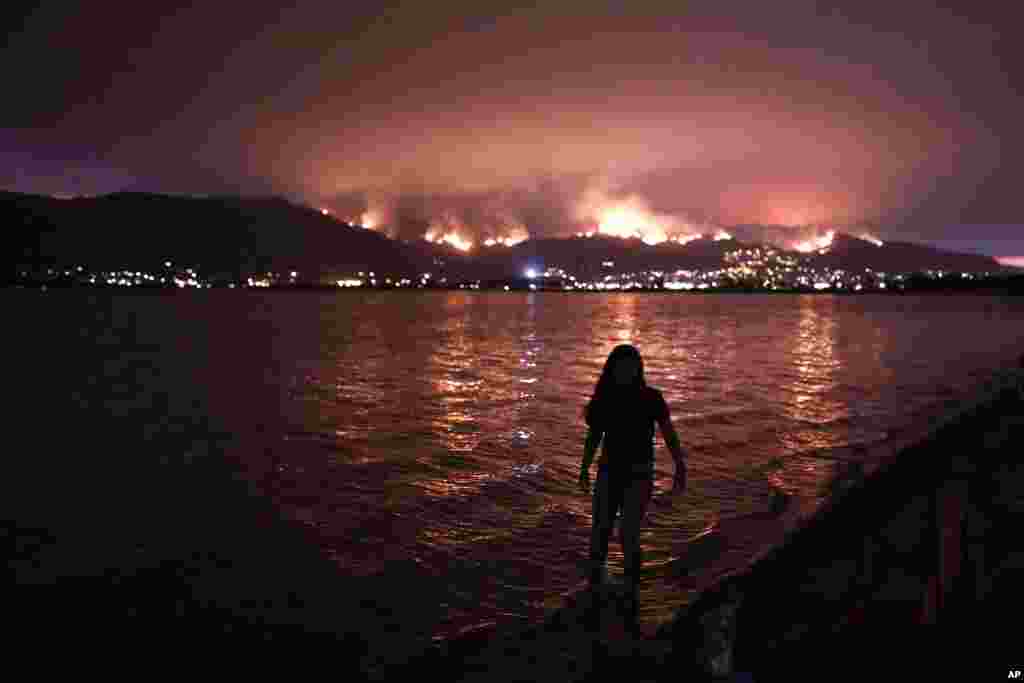 A girl walks through water while watching a wildfire burn in the Cleveland National Forest in Lake Elsinore, California.