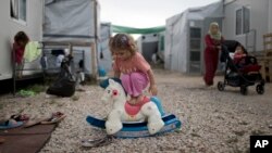 FILE - A Syrian child plays with a plastic toy horse at the refugee camp of Ritsona about 86 kilometers (53 miles) north of Athens, May 25, 2017.