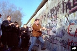 An unidentified West Berliner swings a sledgehammer, trying to destroy the Berlin Wall near Potsdamer Platz, on November 12, 1989, where a new passage was opened nearby. (AP Photo/John Gaps III)