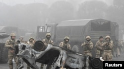 اعتراضات در آلماتی و نیروهای امنیتی پشت خودرویی سوخته - ۱۶ دی ۱۴۰۰
