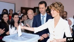 A handout picture released by the official Facebook page of Syria's First Lady Asma al-Assad shows Syrian President Bashar al-Assad (C) watching on as his wife Asma casts her vote at a polling station in Maliki.