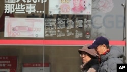 Residents walk past board highlighting the security markers on the latest Yuan note outside a bank in Beijing, China, Nov. 24, 2016.