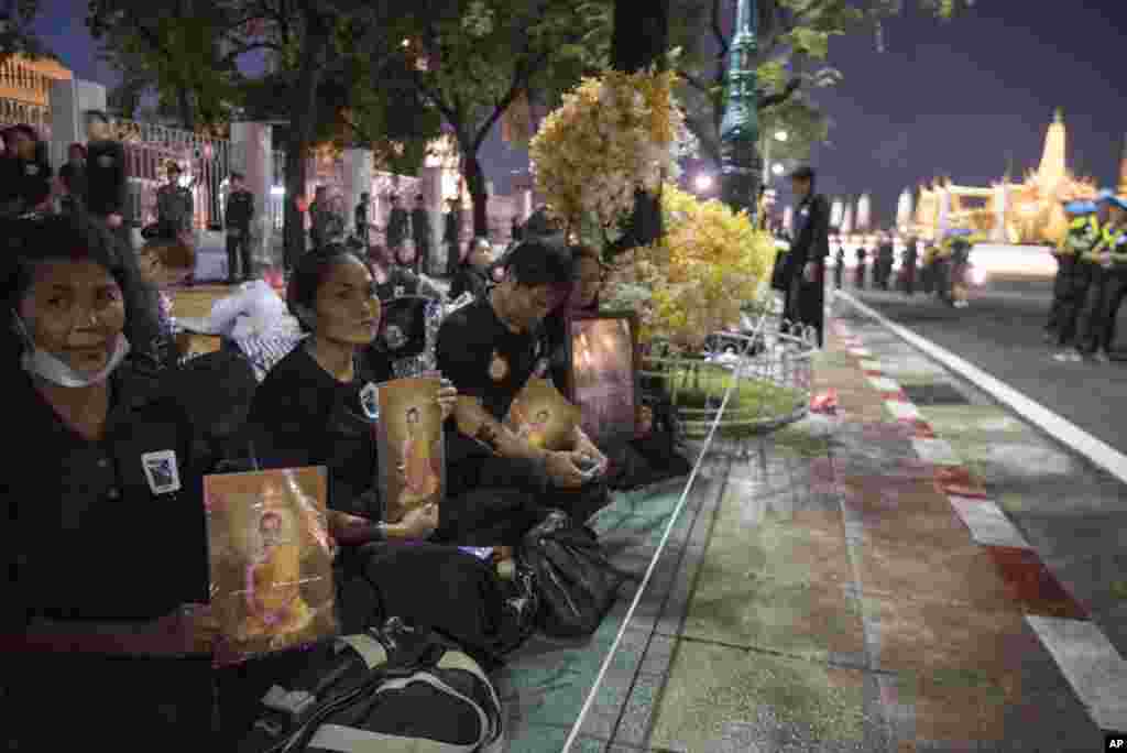 Thai mourners sit with portraits of the late King Bhumibol Adulyadej near Grand Palace to take part in the Royal Cremation ceremony in Bangkok, Thailand, Wednesday, Oct. 25, 2017. (AP Photo/Kittinun Rodsupan)
