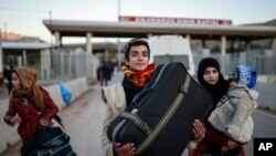 Members of a Syrian family carry their belongings after they crossed into Turkey at the Cilvegozu border gate with Syria, near Hatay, southeastern Turkey, Dec, 18, 2016.