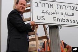 En esta foto publicada por la Municipalidad de Jerusalén, el alcalde de Jerusalén, Nir Barkat, posa con una nueva señal de tráfico en la nueva Embajada de EE.UU. en Jerusalén, Israel, el 7 de mayo de 2018.