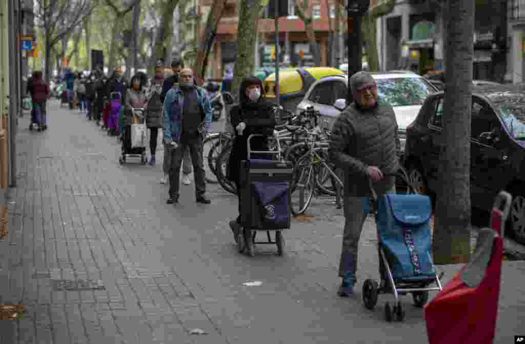 People line up to buy supplies from a shop during the coronavirus outbreak in Barcelona, Spain.