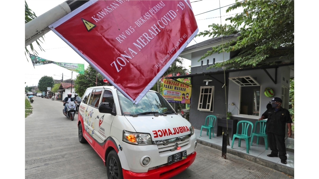 Ambulans yang membawa jenazah korban COVID-19 melewati papan bertuliskan "Zona Merah COVID-19", dalam perjalanan menuju pemakaman di Bekasi di pinggiran Jakarta, 11 Juli 2021. (AP)