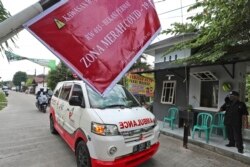 Ambulans yang membawa jenazah korban COVID-19 melewati papan bertuliskan "Zona Merah COVID-19", dalam perjalanan menuju pemakaman di Bekasi di pinggiran Jakarta, 11 Juli 2021. (AP)