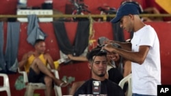 En esta foto del 8 de marzo de 2018, el venezolano Leonardo Wilfredo corta el pelo de un cliente en su barbería improvisada dentro de un refugio para migrantes en el gimnasio Tancredo Neves en Boa Vista, estado de Roraima, Brasil. Un juez federal bloqueó el ingreso de venezolanos por tierra a Brasil el domingo 5 de agosto de 2018.