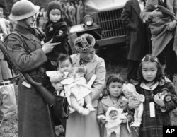 FILE - Cpl. George Bushy, left, a member of the military guard which supervised the departure of 237 Japanese people for California, holds the youngest child of Shigeho Kitamoto, center, as she and her children are evacuated from Bainbridge Island, Wash.,