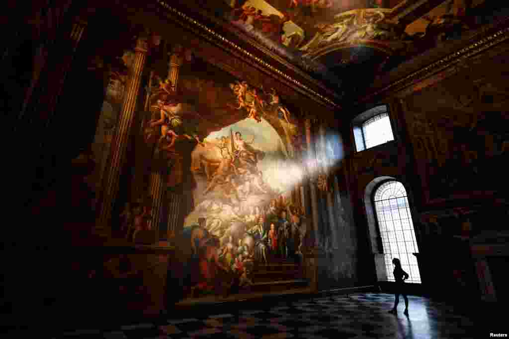 A gallery assistant poses beside a fresco during the reopening of The Painted Hall, Old Royal Navy College in London, Britain.