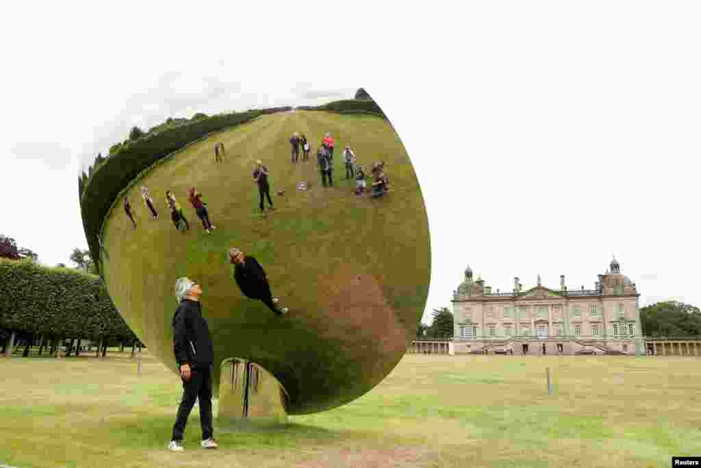 British-Indian artist Anish Kapoor is reflected in one of his sculptures as he poses for photographs in the gardens at Houghton Hall in Norfolk, Britain.