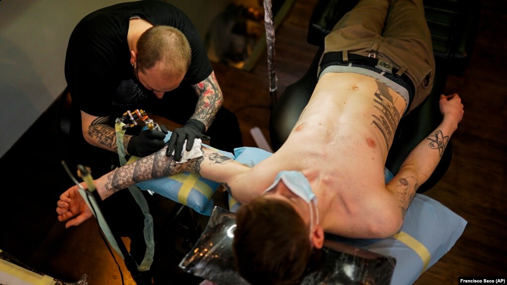 A man, wearing a protective face covering to prevent the spread of coronavirus, is tattooed at Paul and Friends tattoo store in downtown Brussels, March 26, 2021. (AP Photo/Francisco Seco, File)