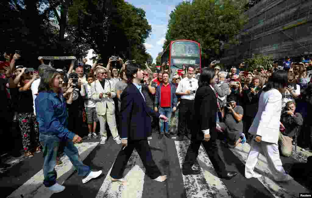 People take pictures as the Beatles cover band members walk on the crossing on Abbey Road in London to mark the 50th anniversary of the day the Beatles were photographed on it.