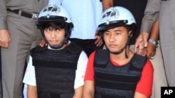 Workers from Myanmar, Saw, left, and Win, sit together, escorted by a Thai police officer, during a press conference in Koh Tao island, Surat Thani province, Thailand, Friday, Oct. 3, 2014.