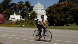 A woman on a bicycle rides along the car-free John F. Kennedy Drive in Golden Gate Park with the Conservatory of Flowers in the background, Wednesday, April 28, 2021, in San Francisco. (AP Photo/Eric Risberg)