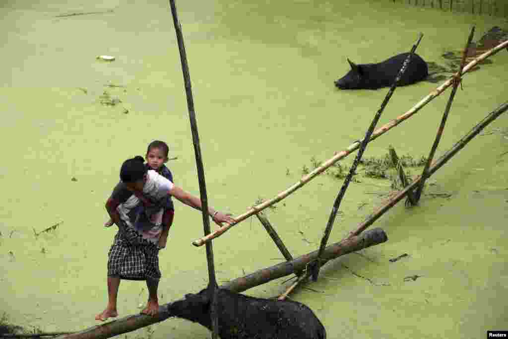 A villager carrying a child uses a makeshift bamboo bridge to cross a flooded area in the Jorhat district, in the northeastern Indian state of Assam.