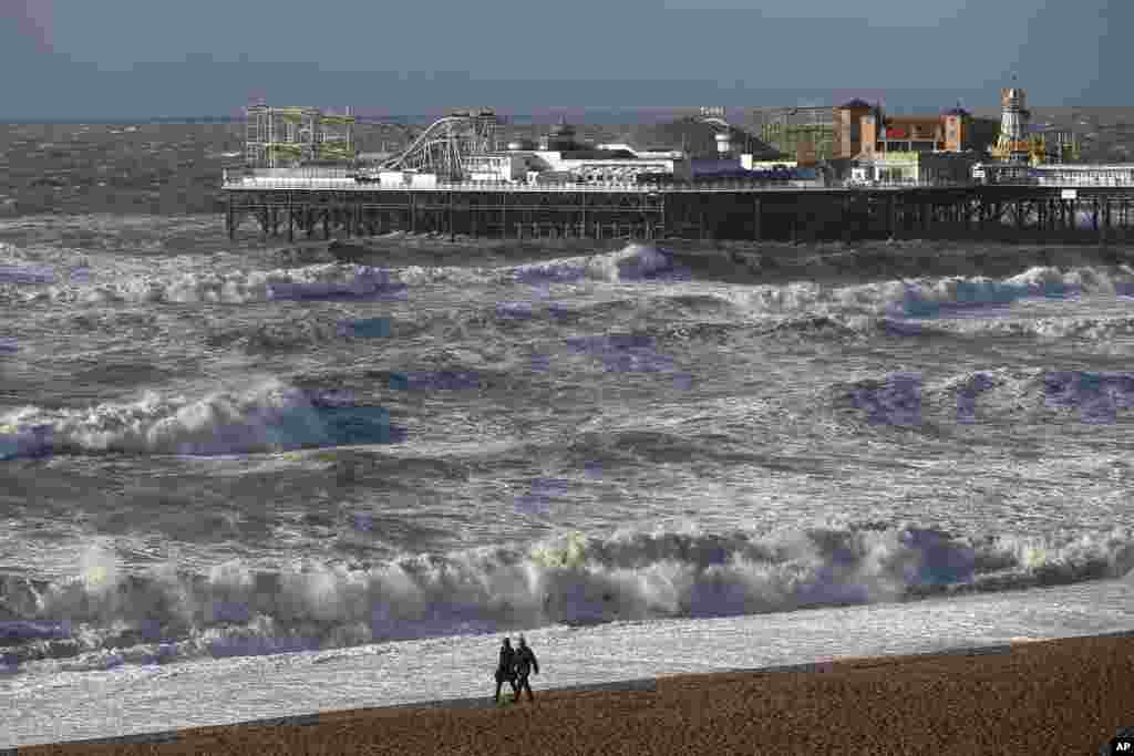 People walks along the shoreline as waves crash onto the beach in Brighton, England, Oct. 28, 2013.