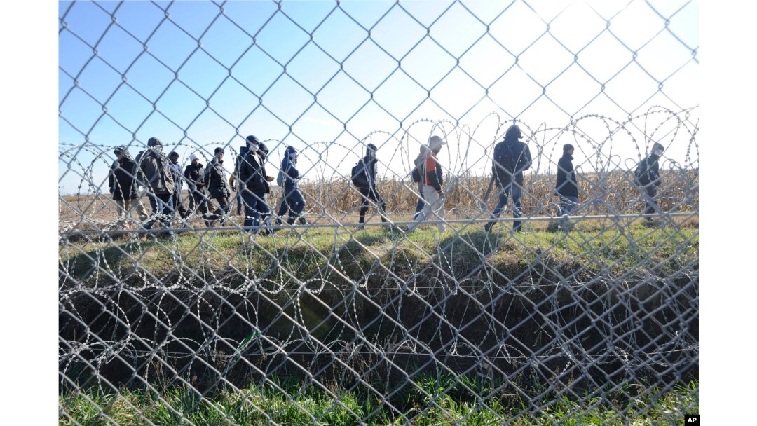FILE - Migrants walk behind a temporary protective fence at the border between Hungary and Serbia near Morahalom, southeast of Budapest, Hungary, Feb. 22, 2016.