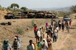 FILE - Villagers return from a market to Yechila town in south central Tigray walking past scores of burned vehicles, in Tigray, Ethiopia, July 10, 2021.