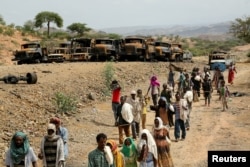 FILE - Villagers return from a market to Yechila town in south central Tigray walking past scores of burned vehicles, in Tigray, Ethiopia, July 10, 2021.