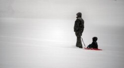 Un hombre y su hijo se dirigen a una colina en un parque del suroeste de la ciudad de Roanoke para divertirse en la nieve el domingo 16 de enero de 2022 en Roanoke, Virginia.