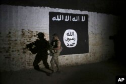 FILE - An Iraqi soldier inspects a train tunnel, adorned with an Islamic State group flag, that was used as training camp for IS fighters, in western Mosul, Iraq, March 1, 2017. IS has since been being rolled up territorially in both Iraq and Syria.