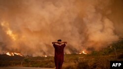 A woman looks at wildfires tearing through a forest in the region of Chefchaouen in northern Morocco on 8.15.2021