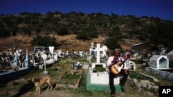 A musician sits on a tomb in the Valle de Chalco municipal cemetery as people begin to arrive to pay their respects to their dead, on the outskirts of Mexico City, Oct. 31. 2021.