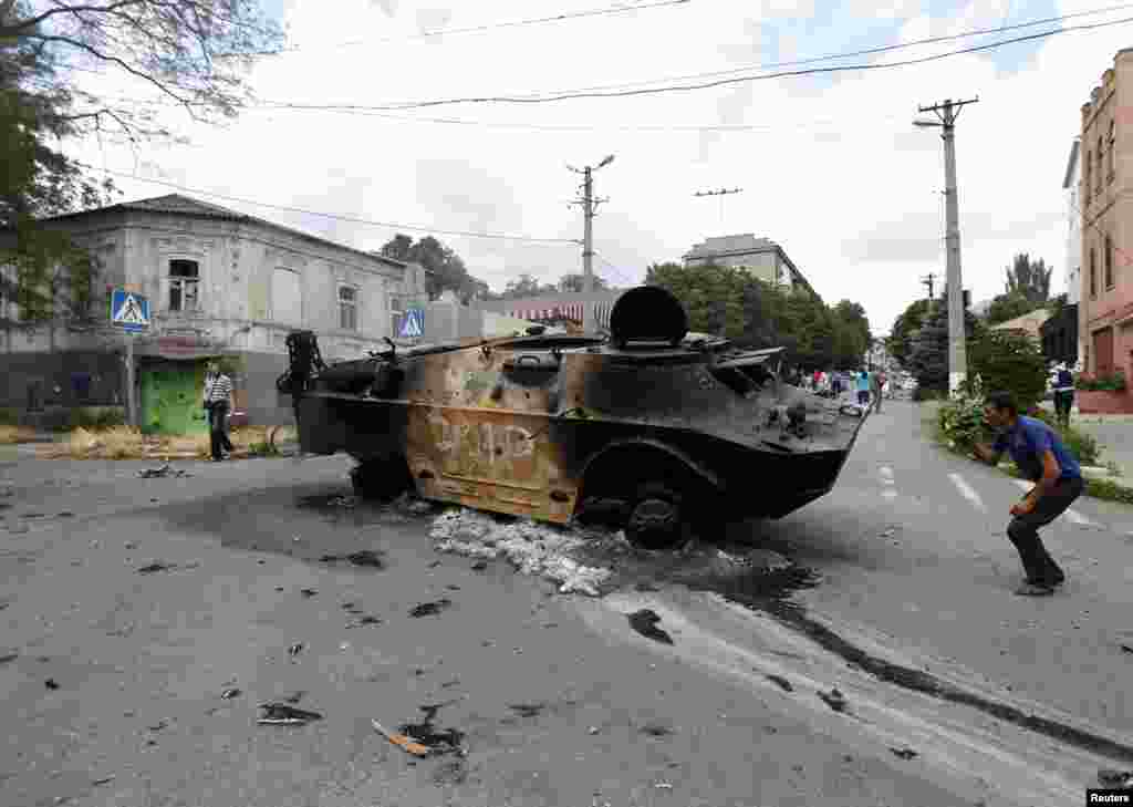Residents look at a destroyed armored personnel carrier of the DNR (Donetsk People's Reublic), Mariupol, June 13, 2014. 